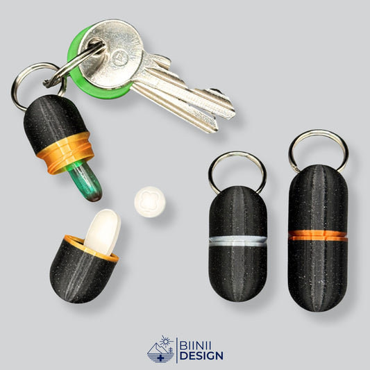 Elegant black keychain pill holder with gold accent on keys, opened to show compact capacity for daily medication. Premium travel pill case by Biinii Design.