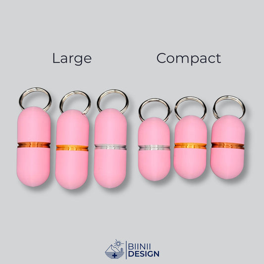 Deluxe keychain pill case lineup: Large (copper, gold, silver rings) next to Compact (silver, gold, copper rings). Solid pink finish, two sizes.