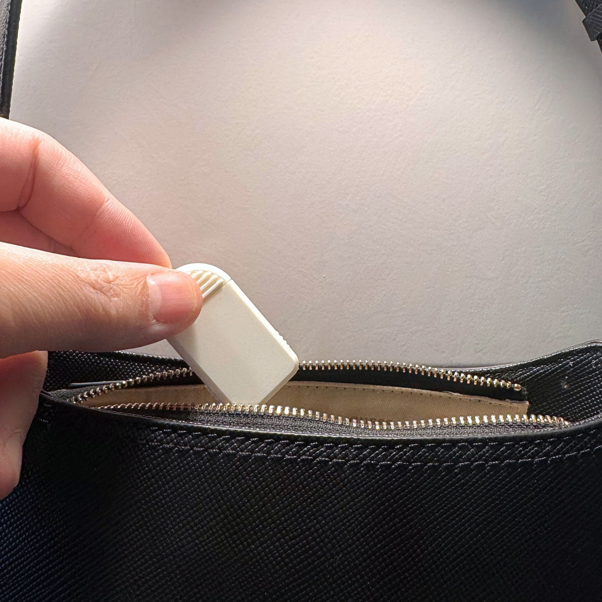 Compact 2-Compartment Pill Box (Monochrome White) being placed into a leather handbag. Highlights extreme portability and discreet travel solution.