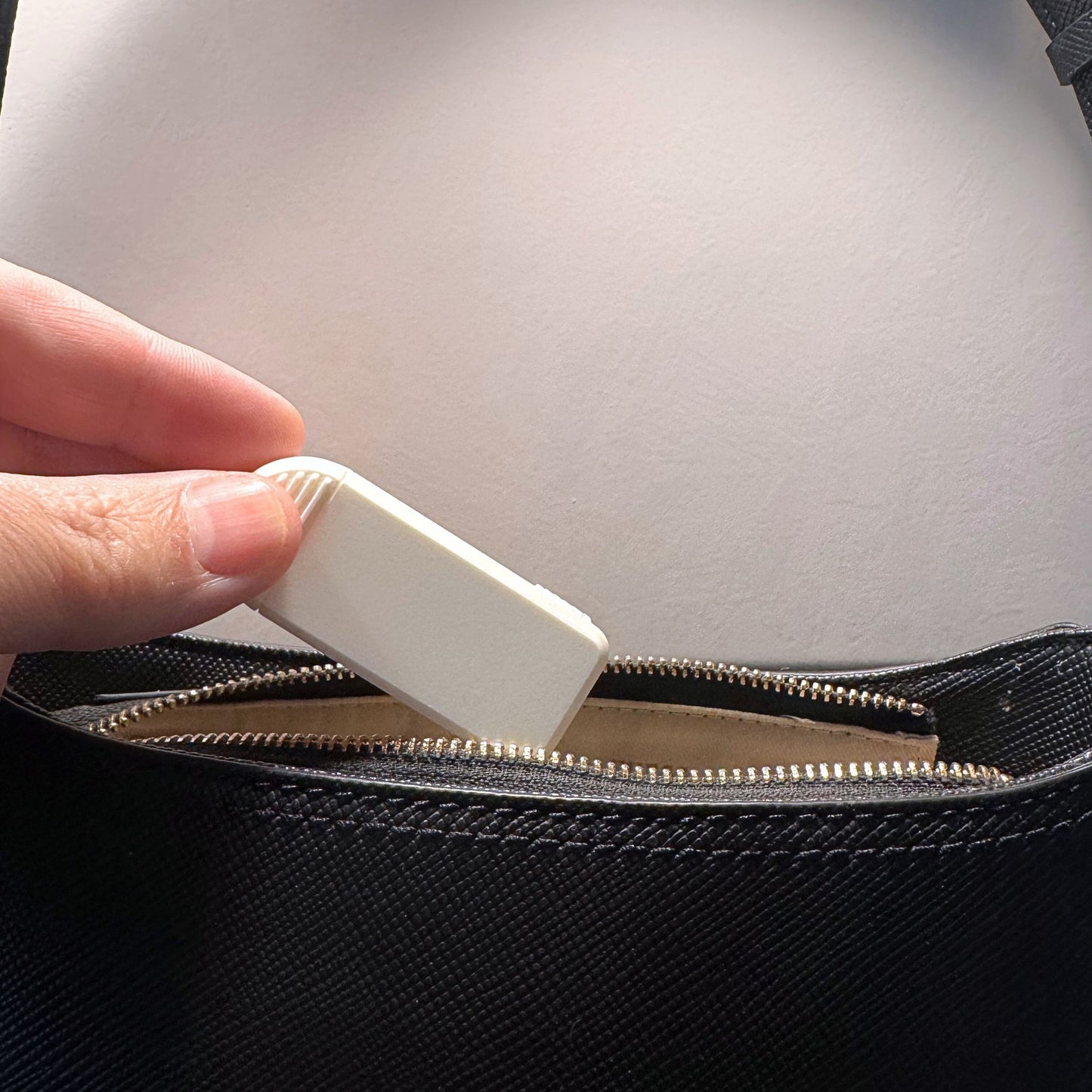 Compact 3-Compartment Pill Box (Monochrome White) being placed into a leather handbag. Highlights extreme portability and discreet travel solution.