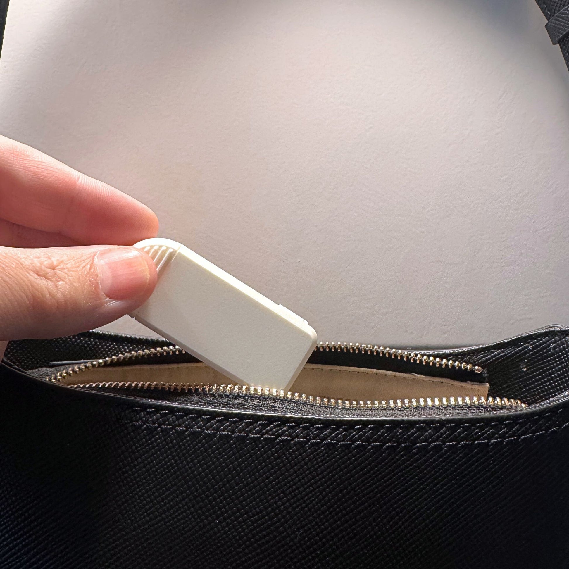 Compact 3-Compartment Pill Box (Monochrome White) being placed into a leather handbag. Highlights extreme portability and discreet travel solution.