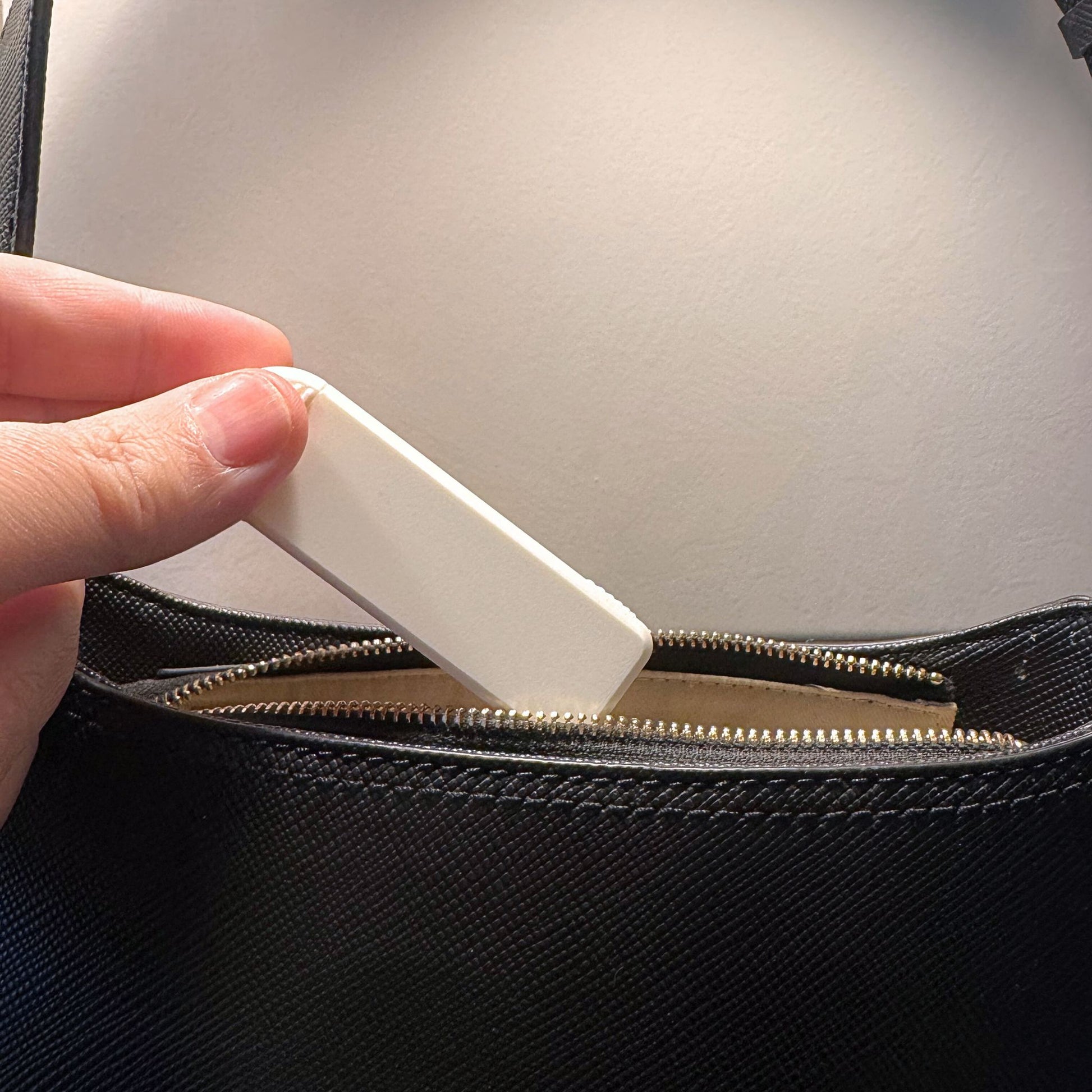 Compact 4-Compartment Pill Box (Monochrome White) being placed into a leather handbag. Highlights extreme portability and discreet travel solution.