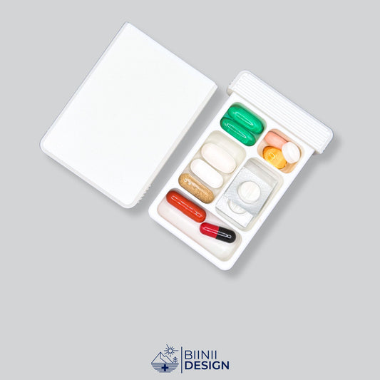 A versatile 5-compartment pill organizer shown open, its hybrid layout filled with daily supplements and vitamins. A Swiss-made Biinii Design piece.