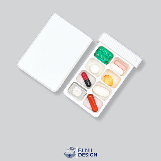 A high-capacity 8-compartment pill organizer shown open, filled with supplements for a one-week trip. A Swiss-made Biinii Design piece.