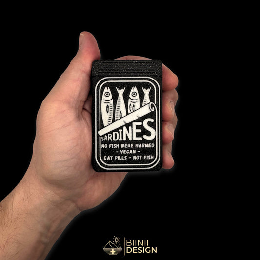 Sardines pill box in galaxy black held in hand for scale. Pocket-sized daily pill organizer with graphic top design.