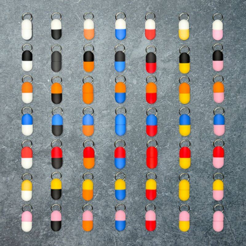 The 49 color combinations of the compact keychain pill holder, seven lid colors by seven base colors, laid out in a grid on slate.