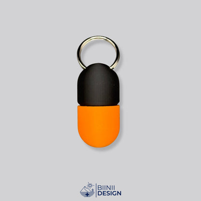 Zweifarbige Compact-Pillendose für den Schlüsselanhänger, Oberteil in Schwarz und Unterteil in Orange.