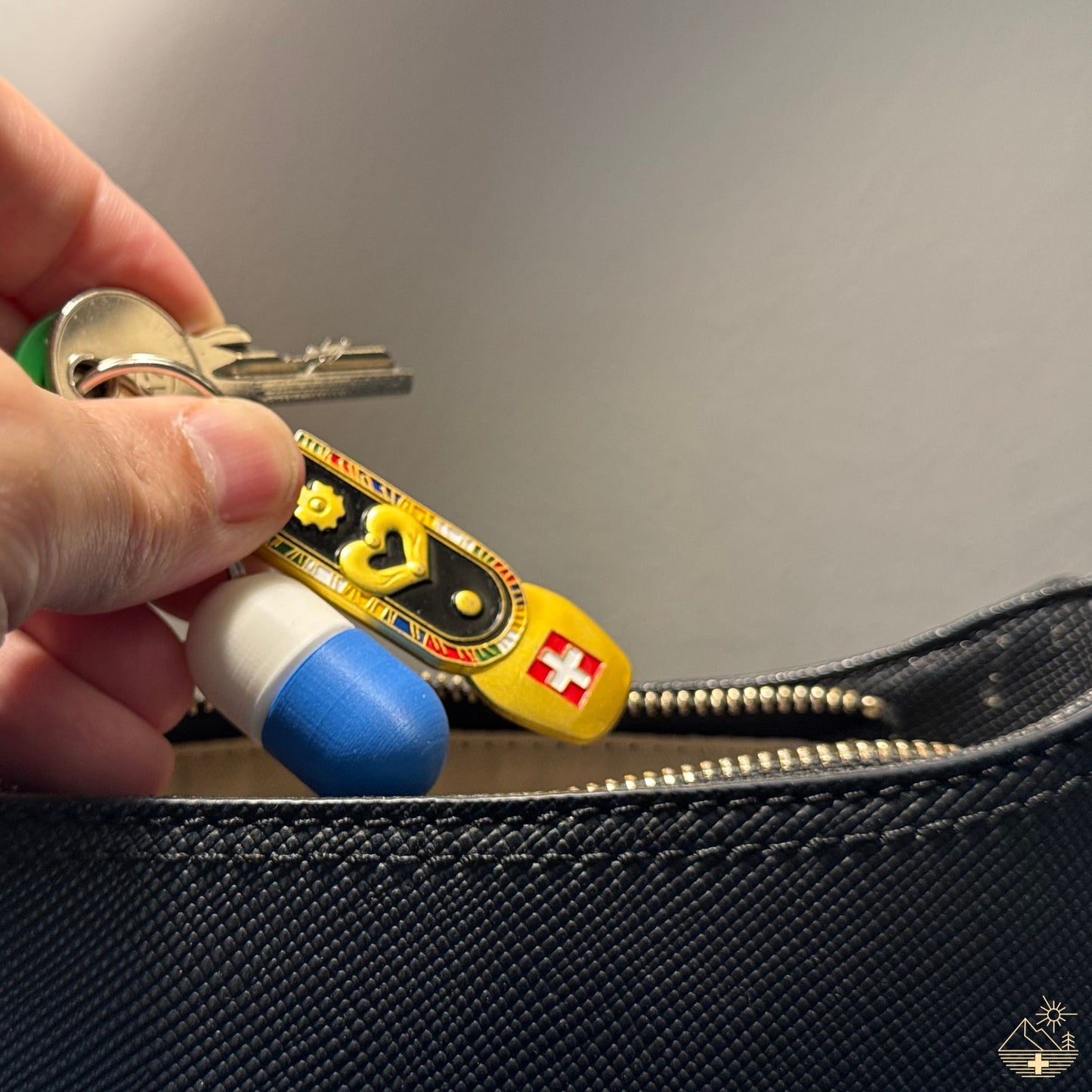 Compact Keychain Pill Holder (White/Blue) inserted discreetly into a blue leather handbag. Swiss flag key ring highlights feminine, discreet EDC.