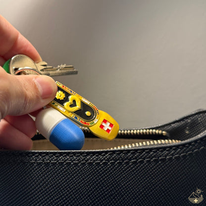 Weiß-blaue Compact-Pillendose für den Schlüsselanhänger mit Metallring, in eine blaue Lederhandtasche gesteckt.