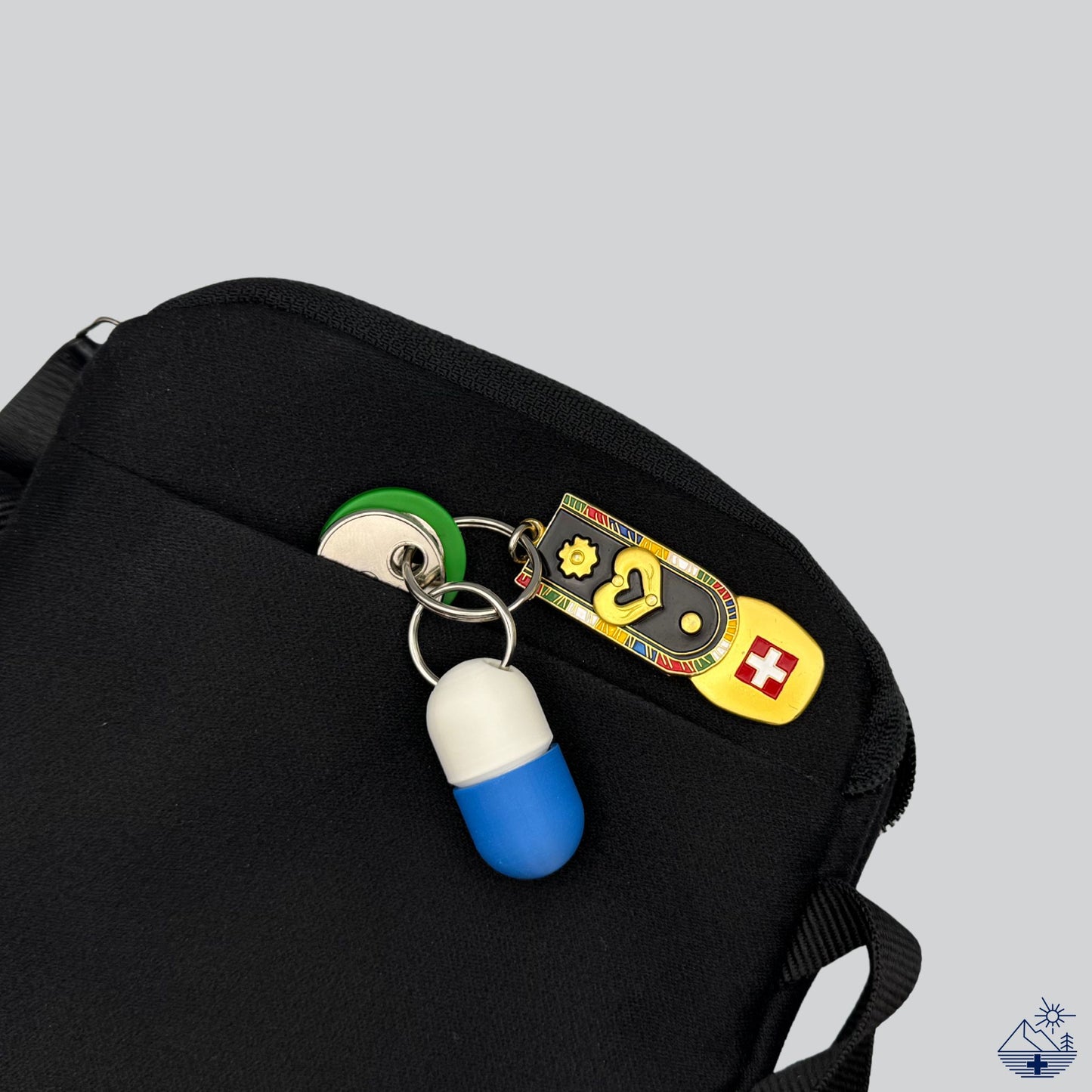 Compact Keychain Pill Holder (White/Blue) attached to keys, discreetly tucked in a men's pouch. Swiss flag key ring enforces Premium Swiss-made EDC concept.