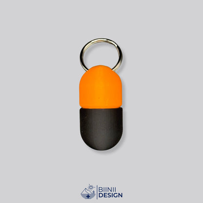 Zweifarbige Compact-Pillendose für den Schlüsselanhänger, Oberteil in Orange und Unterteil in Schwarz.