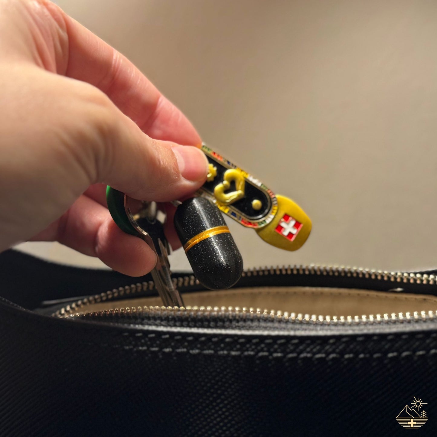 Black keychain pill case with gold accent on Swiss flag keyring, placed into handbag. Discreet, Swiss-made design for everyday carry.