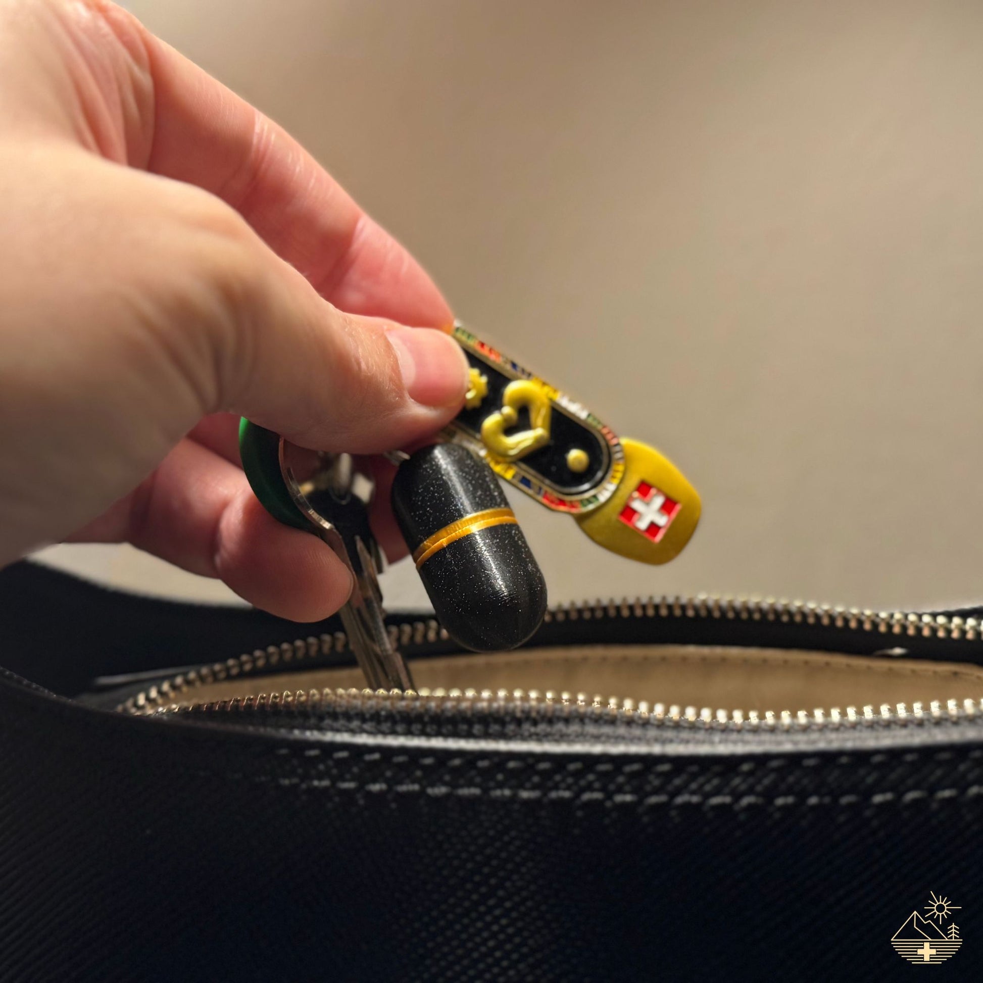 Black keychain pill case with gold accent on Swiss flag keyring, placed into handbag. Discreet, Swiss-made design for everyday carry.