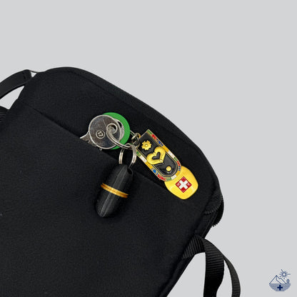 Pilulier porte-clés Deluxe galaxy black à accent doré sur son anneau métallique, glissé dans une sacoche.