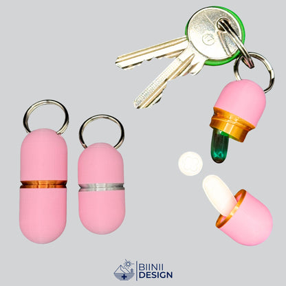 Offene Deluxe-Pillendose in zartem Rosa an Schlüsseln, ein Softgel oben, eine weiße längliche Tablette unten, daneben Compact in Silber und Large in Kupfer.