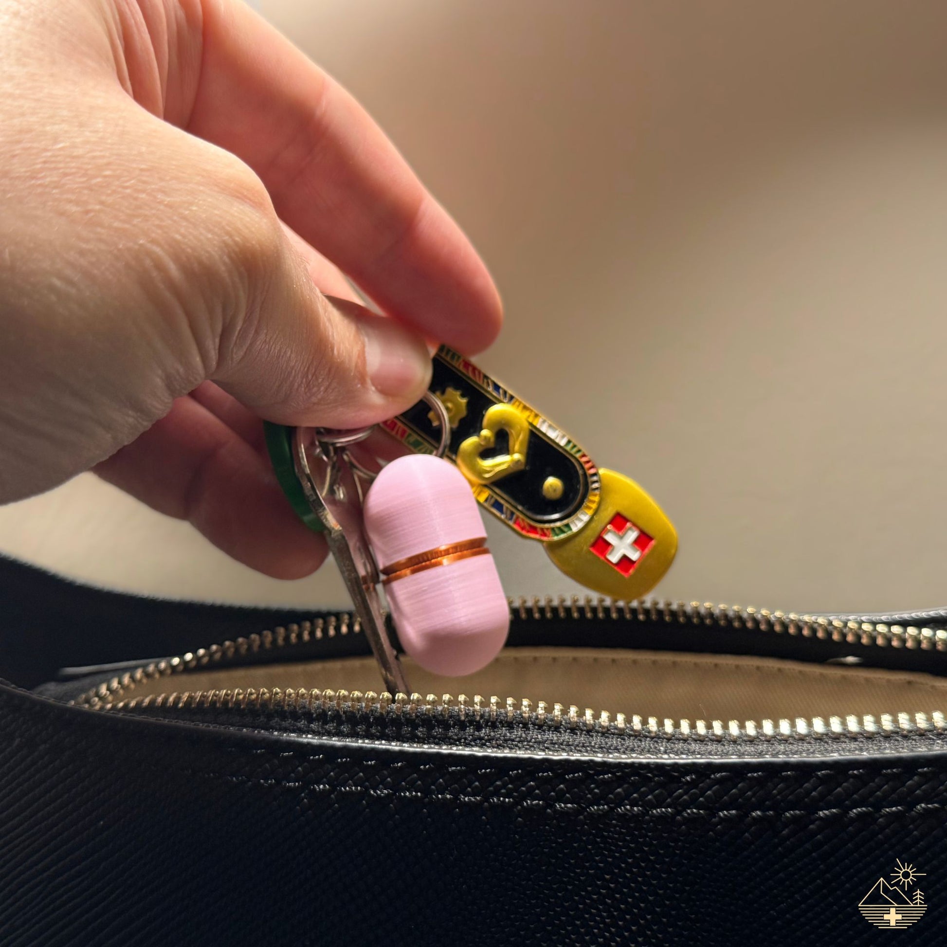 Elegant pink keychain pill case (copper ring) being inserted into a leather handbag. Discreet daily medication holder for travel or handbag.