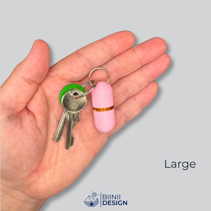 Large-Deluxe-Pillendose in zartem Rosa mit Kupfer-Akzent an Schlüsseln, in der Hand gehalten als Größenvergleich.