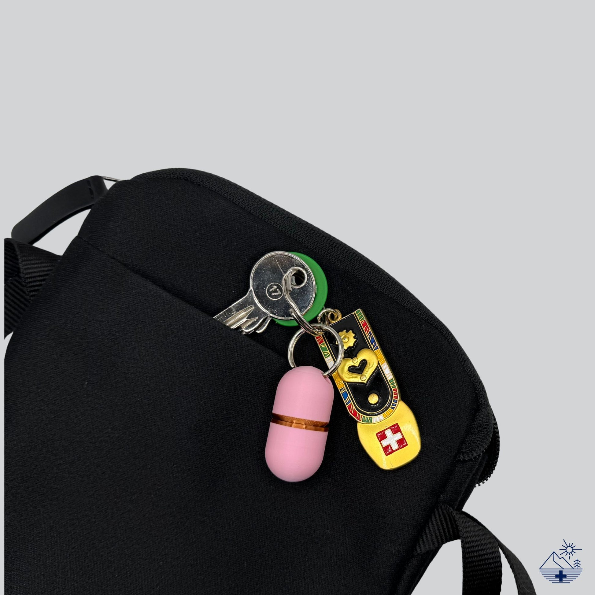 Premium pink keychain pill holder (copper ring) attached to keys, partially tucked into a travel pouch. Compact pill case for short trips and portability.
