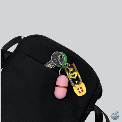 Deluxe-Pillendose in zartem Rosa mit Kupfer-Akzent und einem Anhänger mit Schweizer Flagge, die Schlüssel stecken in einer schwarzen Tasche.