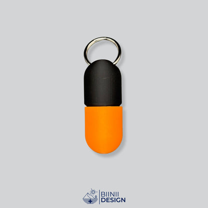 Zweifarbige Large-Pillendose für den Schlüsselanhänger, Oberteil in Schwarz und Unterteil in Orange.
