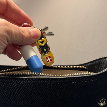 Weiß-blaue Large-Pillendose für den Schlüsselanhänger mit Metallring, in eine blaue Lederhandtasche gesteckt.