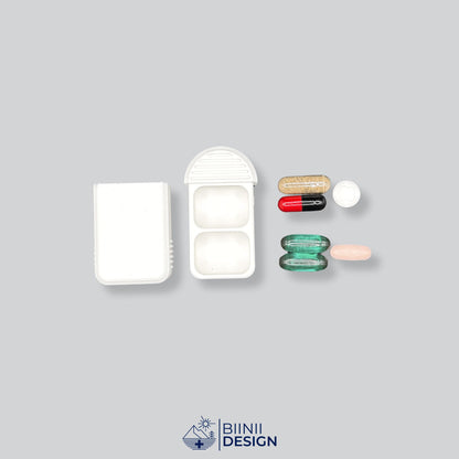 Pilulier compact 2 compartiments blanc ouvert à côté de comprimés, gélules et compléments à répartir en doses du matin et du soir.