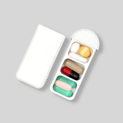 Compact Swiss-made pill organizer with three compartments, shown open with mixed pills and supplements, featuring a detached sliding lid for clear visibility of its layout.