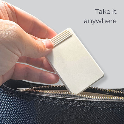 Closed eight-compartment travel pill box slipped into a handbag, flat enough to disappear inside.