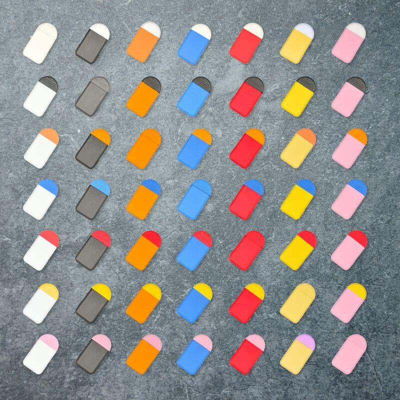 The 49 color combinations of the 2-compartment daily pill organizer, seven lid colors by seven base colors, laid out in a grid on slate.