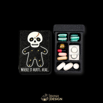 Healing Voodoo art edition pill organizer lid next to its 5-compartment base filled with capsules, silver voodoo doll on galaxy black.
