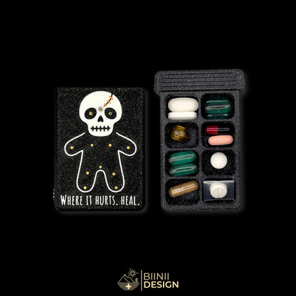 Healing Voodoo art edition pill organizer lid beside a filled 8-compartment base holding tablets, capsules and supplements.