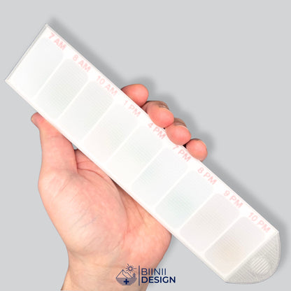 Closed hourly pill organizer held in hand for scale, red hour markings from 7 AM to 10 PM visible through the translucent lid.