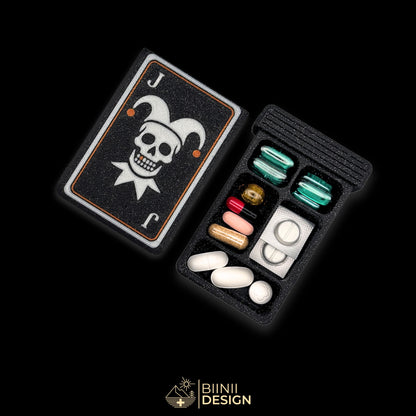 Joker Skull art edition pill organizer: silver jester skull on a playing card with copper accents, on galaxy black, beside a filled 5-compartment base.