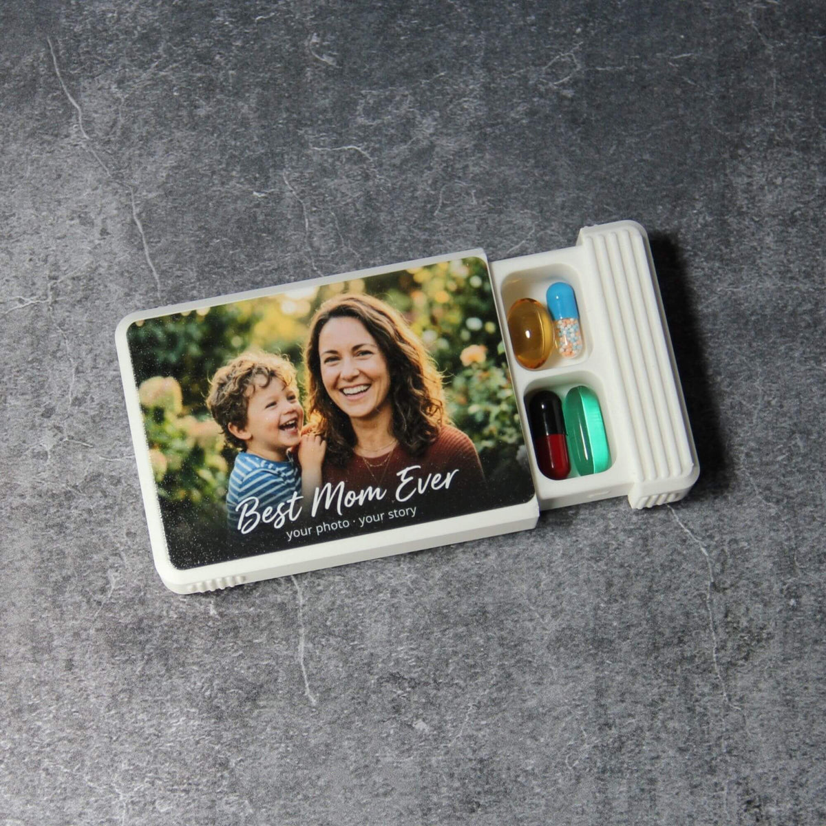 Custom pill organizer with a UV-printed family photo and the words Best Mom Ever on the white lid, lid partly closed to reveal the first row of capsules in the 5-compartment base