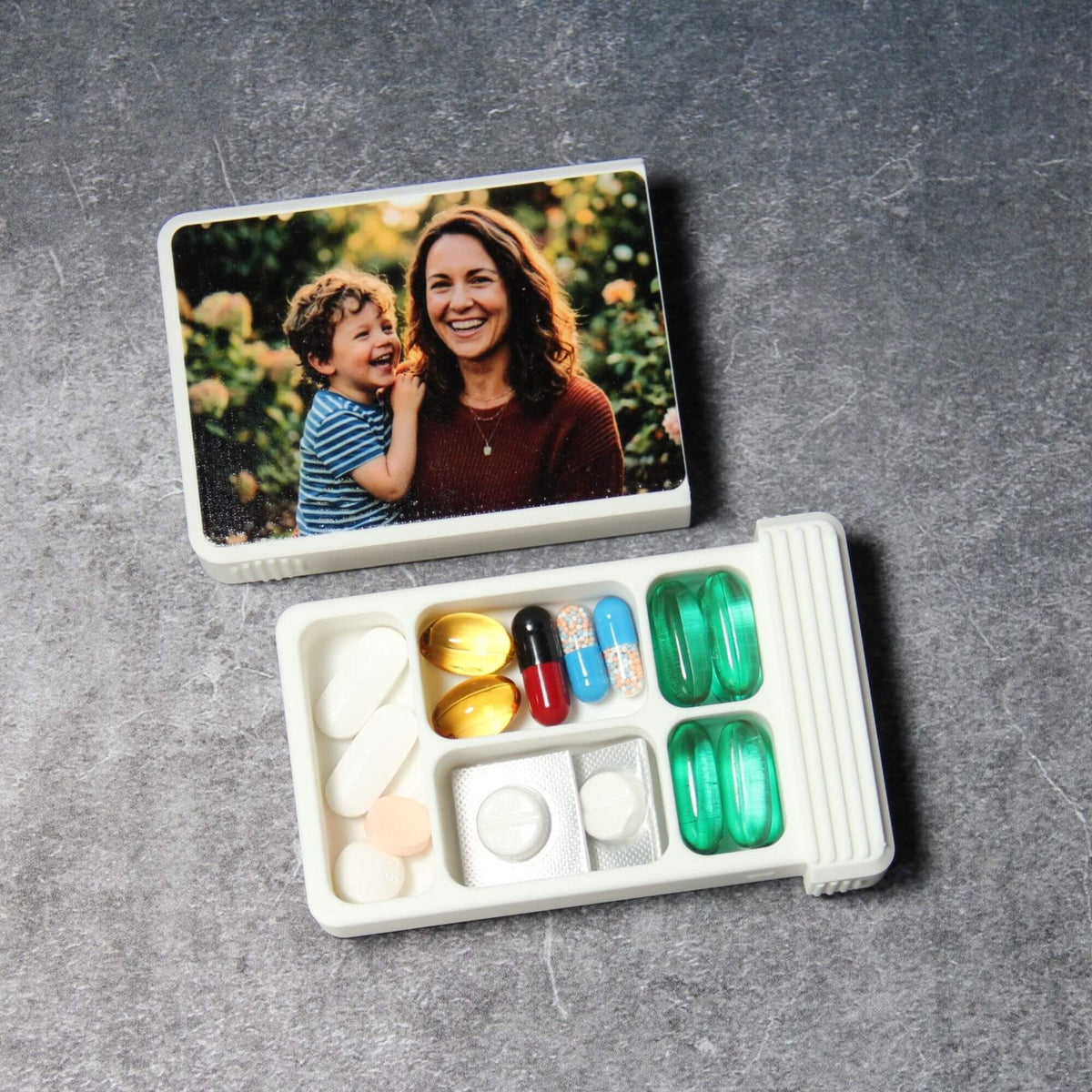 Custom photo pill organizer, white, lid removed: 5-compartment base with a full-width tray, capsules, a cut blister pack and green softgels
