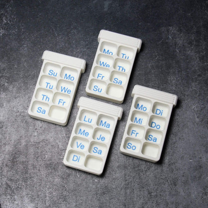 Four white weekly bases of the custom photo pill organizer, days of the week printed in blue into the compartments: English with Sunday or Monday start, French and German