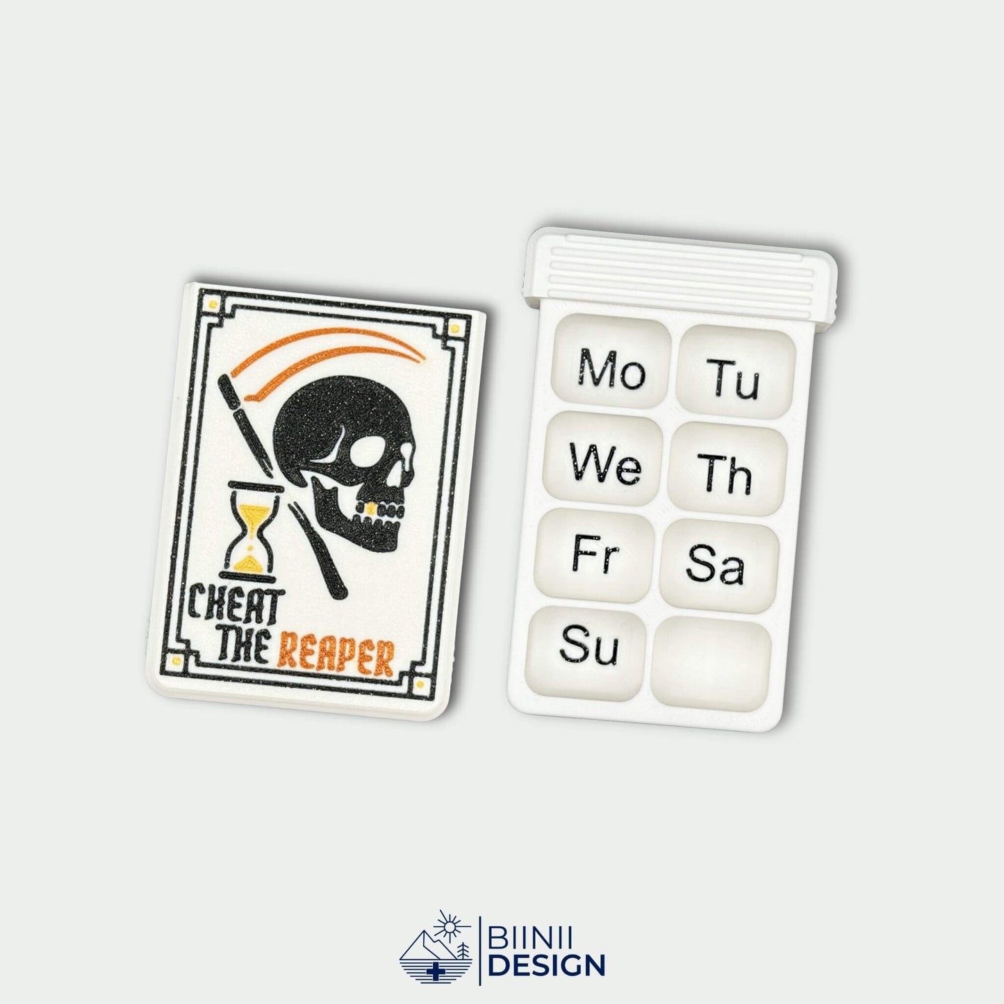 Cheat the Reaper White Edition cover next to white 8-compartment weekly tray with black English Monday start engraving.