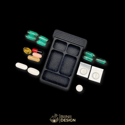 Empty 5-compartment base of the Sardines art edition pill organizer with capsules, cut blister packs and vitamins beside it.