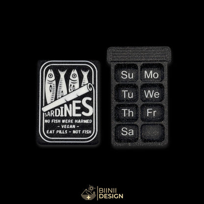 Sardines art edition pill organizer lid next to an empty weekly base, English days printed into the cells, Sunday start.