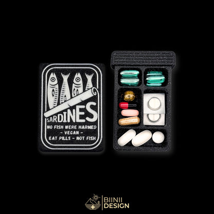 Sardines art edition pill organizer lid next to its 5-compartment base filled with capsules, silver sardine tin on galaxy black.