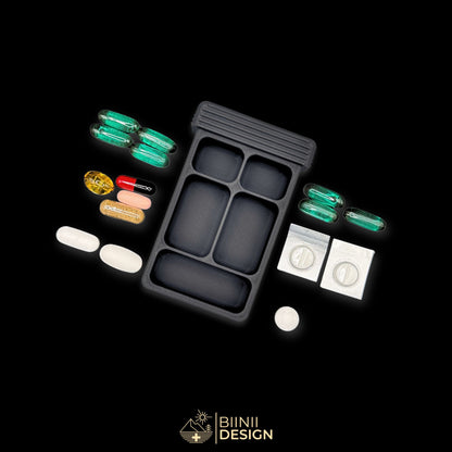 Empty 5-compartment base of the Vulture's Shadow art edition pill organizer with capsules, cut blister packs and vitamins beside it.
