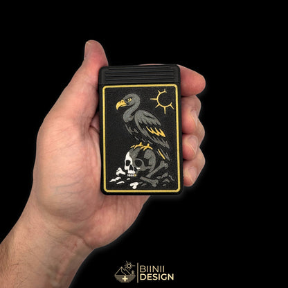 Closed Vulture's Shadow art edition pill organizer held in hand for scale, anthracite vulture, silver skull with its gold tooth, gold frame and sun.
